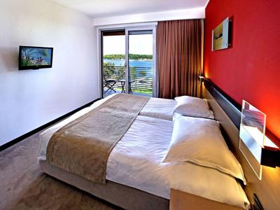 Camera d'hotel moderna con letto matrimoniale, parete rossa e vista su balcone e lago.