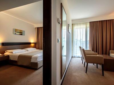 Camera d'hotel moderna con due letti, scrivania, sedie e balcone con tende.