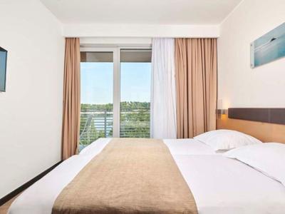 Camera d'hotel moderna con letto matrimoniale, TV e finestra con vista sul paesaggio verde.