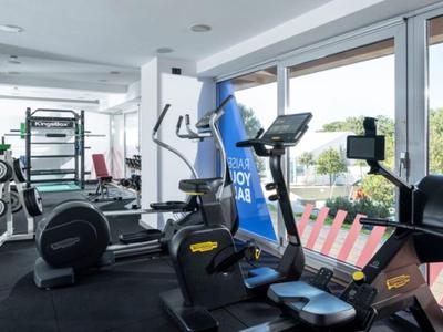 Ein moderner Fitnessraum mit Laufband, Rudergerät und Gewichten neben großen Fenstern mit Aussicht.