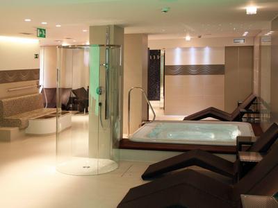 Area benessere moderna con vasca idromassaggio, lettini e zona salotto con luce calda.