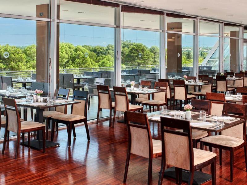 Ristorante luminoso con pavimento in legno e vista sul paesaggio verde attraverso grandi finestre.
