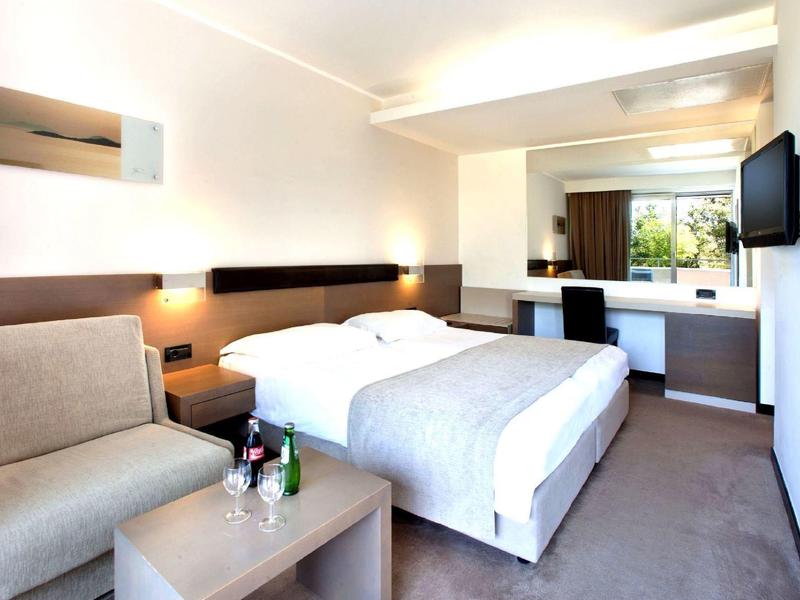 Camera d'hotel moderna con letto matrimoniale, divano, TV e vista sulla terrazza.