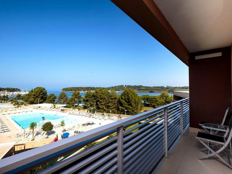 Balcone con vista su una piscina e un paesaggio verde sotto un cielo terso.