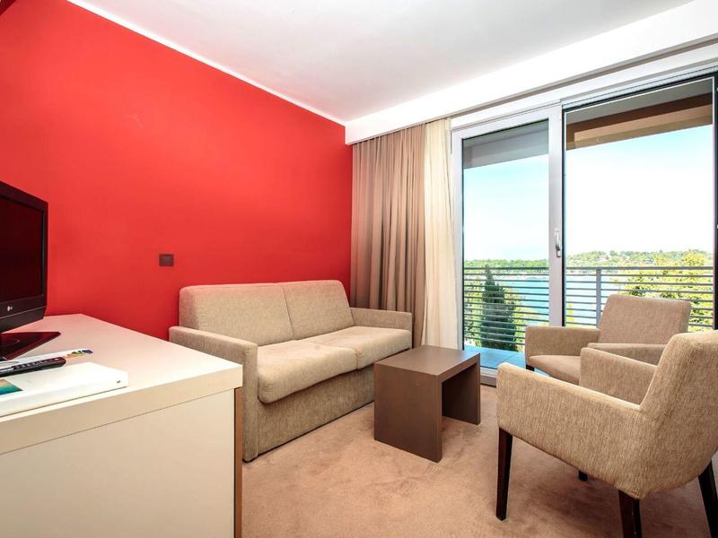 Camera d'hotel accogliente con parete rossa, divano, poltrona e balcone con vista.