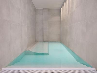 Narrow indoor pool with clear water and gray walls, featuring a minimalist design.