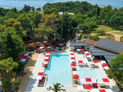 Hotelpool mit roten und weißen Liegestühlen und umliegenden grünen Bäumen.