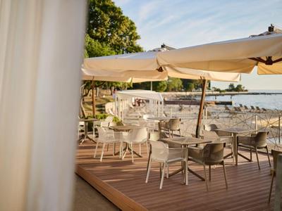 Hotel terrace with tables, chairs, and umbrellas by the water at sunset.