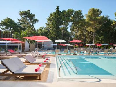 Modern pool area with loungers and red umbrellas in a hotel garden.