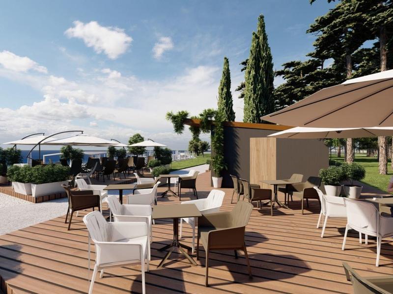 Moderní venkovní prostor s dřevěnou terasou, stoly, židlemi a slunečníky s výhledem na moře.