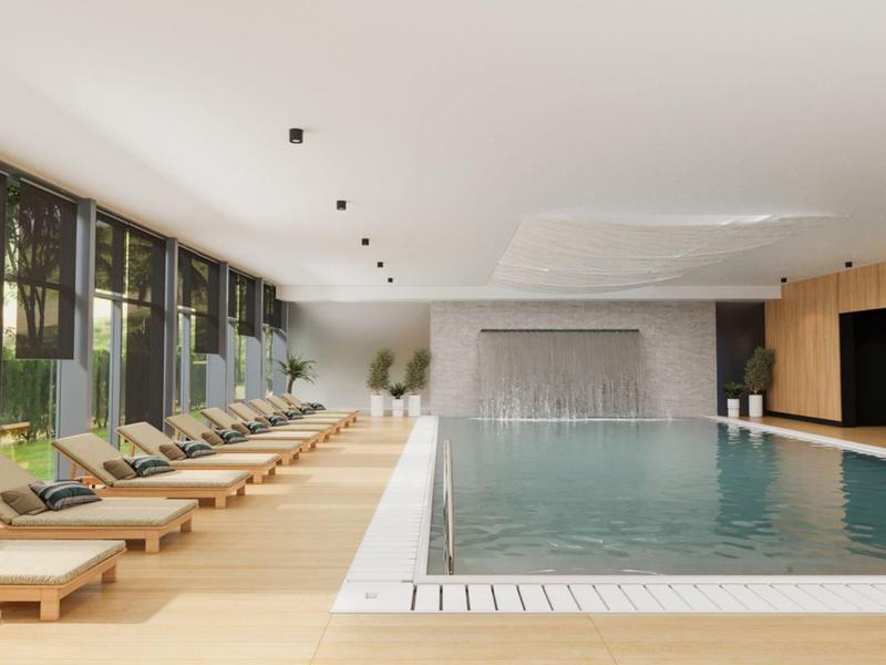 Světle osvětlený vnitřní bazén s lehátky a velkými okny s výhledem na palmy.