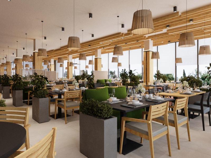 Moderní restaurace se dřevěným nábytkem, zelenými rostlinami a velkými okny s výhledem ven.