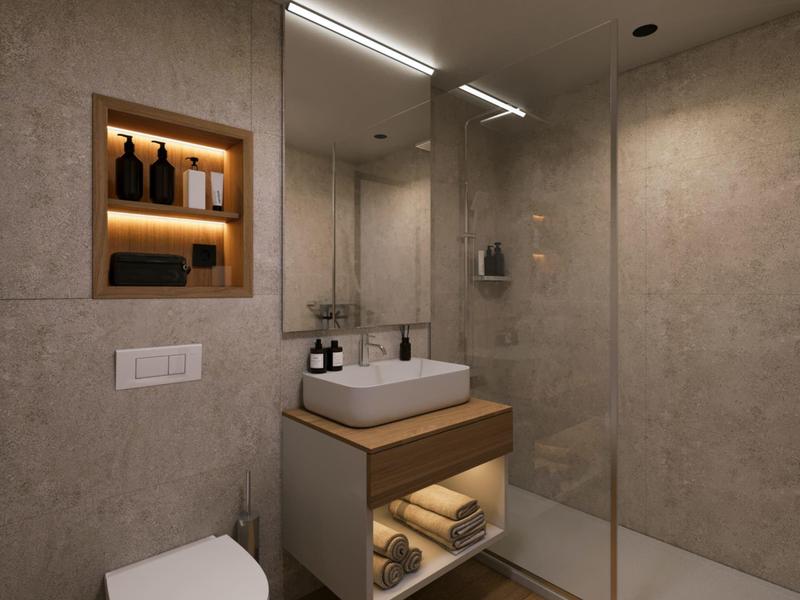 Moderní koupelna s bezbariérovým sprchovým koutem, osvětleným zrcadlem a vestavěnou poličkou na ručníky.