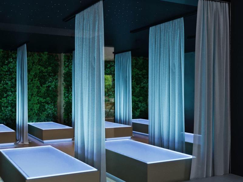 Tmavá spa místnost s bílými oddělenými masážními lehátky a závěsy.