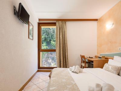 Helles Hotelzimmer mit Doppelbett, Fenster mit Vorhang und Wand-Fernseher.