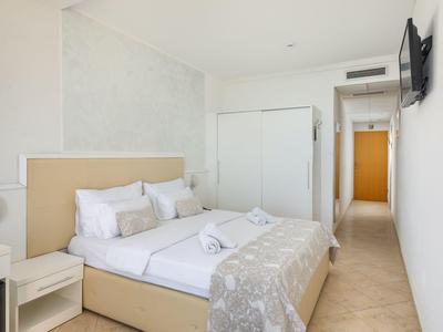 Hell eingerichtetes Hotelzimmer mit Doppelbett, Nachttisch und Fernseher an der Wand.