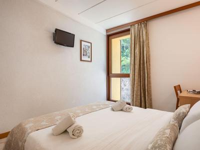 Gemütliches Hotelzimmer mit Doppelbett, Wandfernseher und Fenster mit Vorhang.