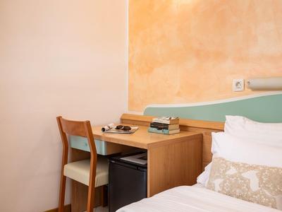 Gemütlicher Hotelzimmerschreibtisch mit Stuhl, Minikühlschrank und Bettrand sichtbar