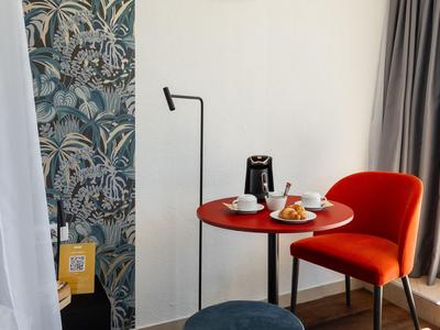 Moderner Essbereich mit rotem Stuhl, rundem Tisch und Kaffeekanne vor weißer Wand und Vorhang.