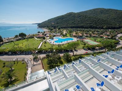 Blick auf ein Hotel mit Pool und Gartenbereich, umgeben von Hügeln und Meer im Hintergrund.