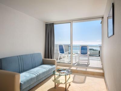 Helles Wohnzimmer mit blauer Couch, kleinem Glastisch und Terrasse mit Meerblick.