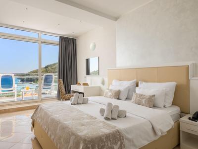 Hell eingerichtetes Hotelzimmer mit Doppelbett, Balkon und Blick auf das Wasser.