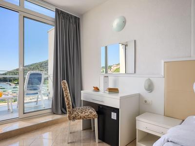 Helles Hotelzimmer mit Schreibtisch, Stuhl und Balkon mit Sitzgelegenheiten und Meerblick.