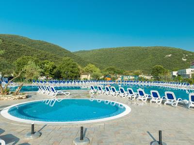 Runder Pool mit Liegestühlen im Freien mit Bergen im Hintergrund.