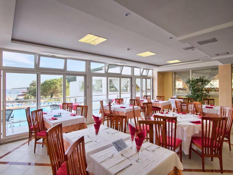 Spacious dining room with wooden chairs and white tablecloths near large windows overlooking the pool.