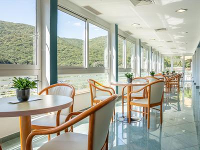 Área de comedor luminosa con mesas, sillas y grandes ventanas con vistas a colinas verdes.