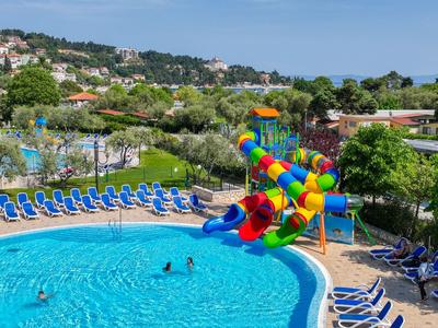Juego de toboganes de agua coloridos en una piscina al aire libre con sillas y vegetación de fondo.