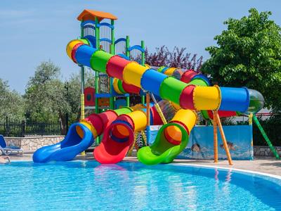 Toboganes acuáticos coloridos se extienden en una piscina con agua azul, rodeada de tumbonas y árboles.