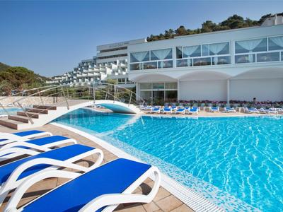 Piscina moderna de hotel con tumbonas azules y un pequeño puente en un día soleado.