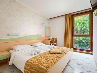 Habitación de hotel luminosa con dos camas individuales, colcha amarilla y vista a árboles verdes por la ventana.