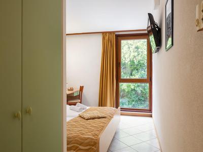 Pequeña habitación de hotel con cama individual, ventana y televisor en la pared.