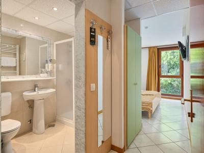 Habitación de hotel con baño, lavabo, inodoro y cama con vista a la ventana.