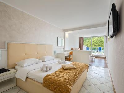 Habitación de hotel luminosa con cama doble, sofá y vista a la terraza y piscina.