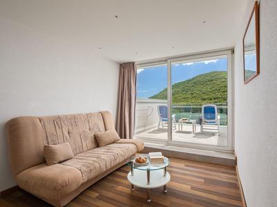 Habitación de hotel moderna con sofá marrón, mesa de vidrio y balcón con vista a colinas verdes.