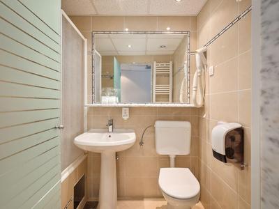 Baño compacto de hotel con lavabo, inodoro y gran espejo sobre el lavabo.