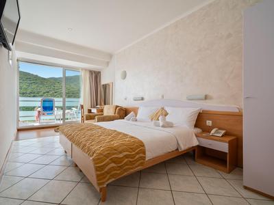 Habitación de hotel luminosa con cama doble, sofá y balcón con vistas al mar.