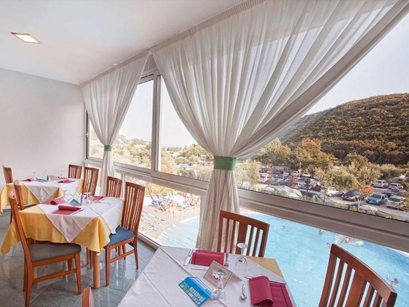Bright restaurant with large windows overlooking pool and hills.