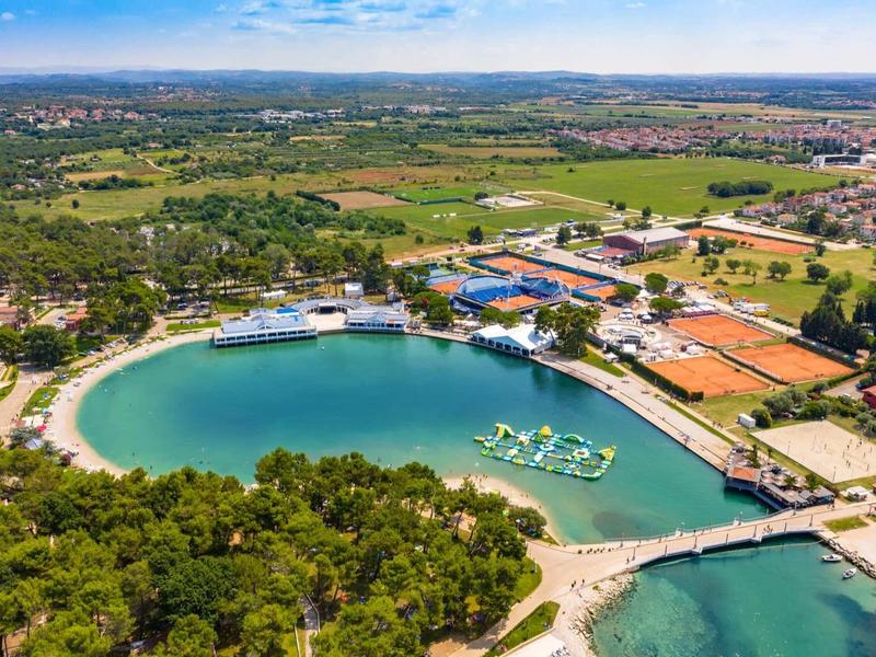 Aerial view of a bay with clear turquoise water, surrounded by greenery and buildings.