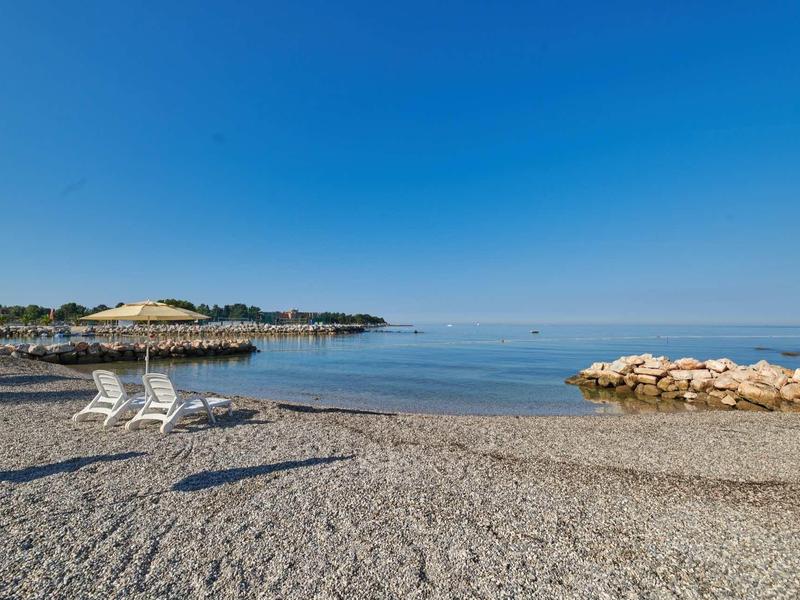 Empty pebble beach with two white lounge chairs under clear blue sky by the sea.