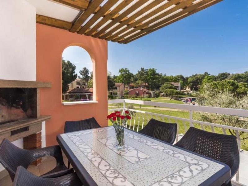 Balcony with dining table, chairs, fireplace, and view of green garden and blue sky.