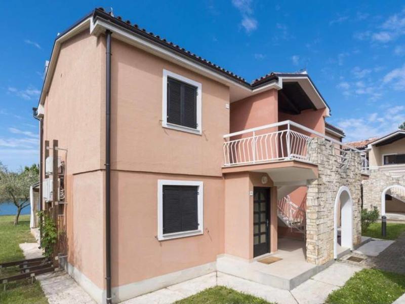Beige holiday house with balcony, stone arch, and blue sky in the background.
