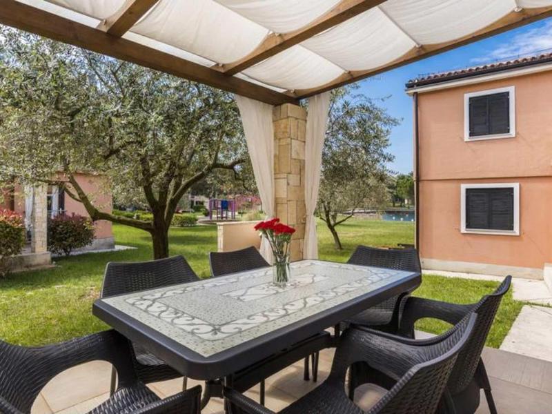 Covered terrace with black garden table and four chairs, view of garden and buildings.