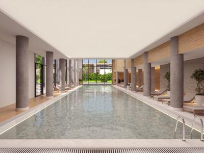 Piscina cubierta moderna y luminosa con columnas, tumbonas y grandes ventanas con vista al jardín.