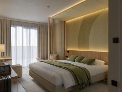 Habitación de hotel moderna con cama grande, iluminación indirecta y ventanas del suelo al techo con cortinas.