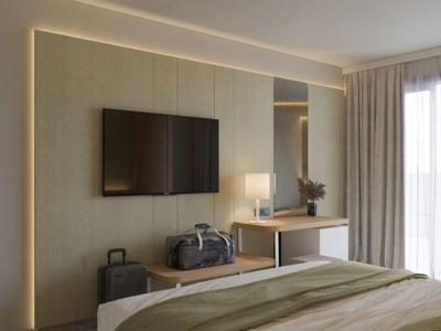 Habitación de hotel moderna con televisor, escritorio, equipaje y cama grande con manta verde.