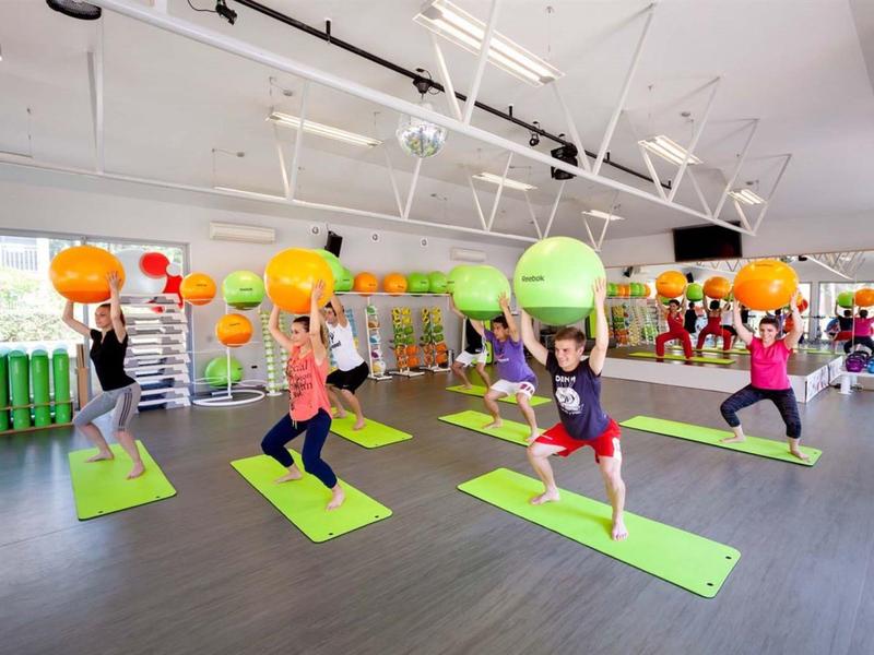 Un grupo de personas practica yoga en un estudio luminoso y moderno con ventanas y pelotas de ejercicio coloridas.